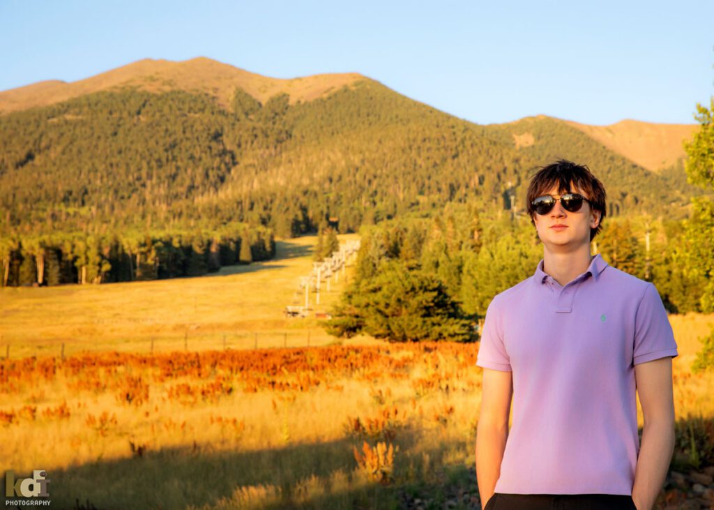 High school senior photos showing boy with brown hair, wearing a purple collared t-shirt and sunglasses, with the San Francisco Peaks in the background, portrait photography in Flagstaff AZ by senior photographer KDI Photography