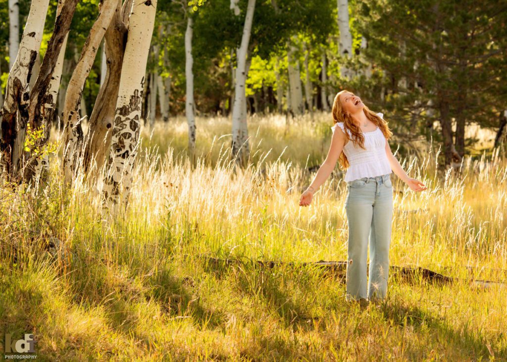 High school senior photos showing girl with red hair, wearing jeans and white shirt, throwing back her head and laughing, in the San Francisco Peaks of Northern Arizona, portrait photography in Flagstaff AZ by senior photographer KDI Photography