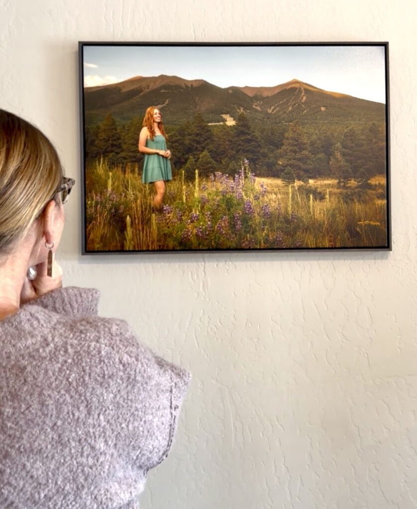 Mother looks at wall art that features high school senior portrait showing girl with red hair, in front of the San Francisco Peaks of Northern Arizona, portrait photography in Flagstaff AZ by senior photographer KDI Photography