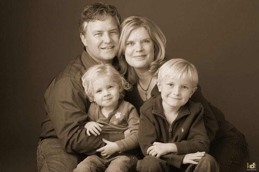 Black and white studio portrait of family of four snuggling and smiling in portrait created by Flagstaff photographer KDI Phiotography