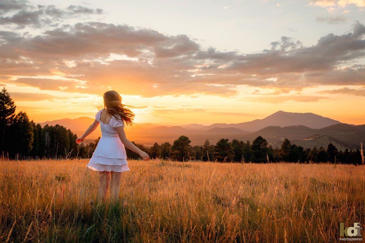 Senior portrait of girl in white dress spinning at sunset in a meadow, senior photos by Flagstaff photographer KDI Photography