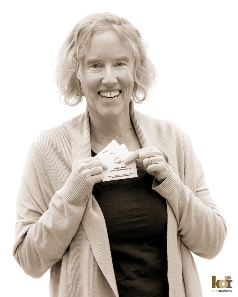 Black and white studio portrait of WENA (Women Empowering Northern Arizona) founder Katie Woodard holding ballots, in portrait with a white background created by Flagstaff photographer KDI Photography