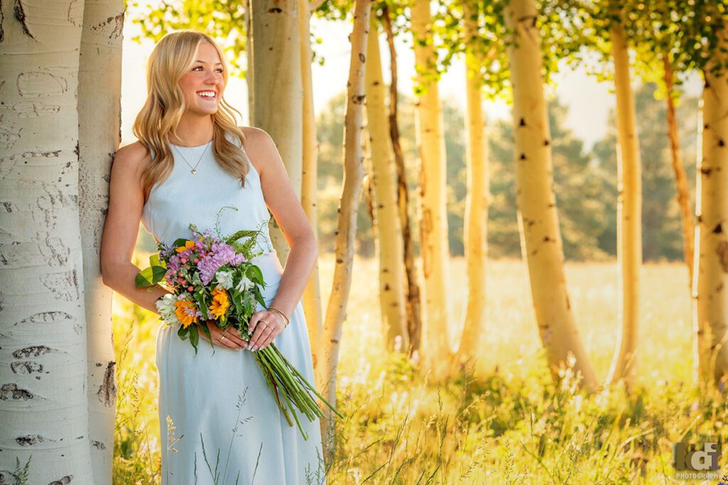 High school senior photos showing girl with blond hair, in blue dress standing in the aspen trees, holding a bouquet of flowers, portrait photography in Flagstaff AZ by senior photographer KDI Photography