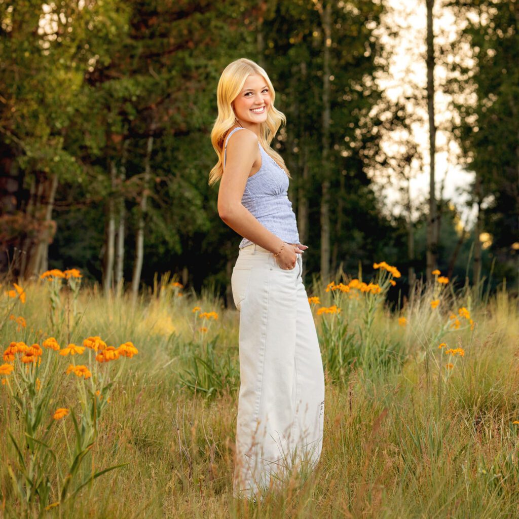 High school senior photos showing girl with blond hair, in white pants and blue tank top among the yellow summer flowers, portrait photography in Flagstaff AZ by senior photographer KDI Photography