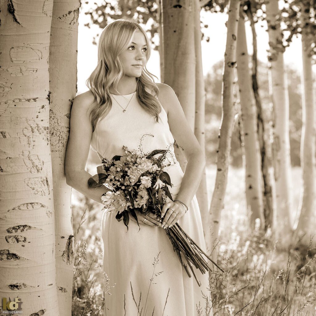 Black and white portrait, high school senior photo showing girl with blond hair, in dress standing in the aspen trees, holding a bouquet of flowers, portrait photography in Flagstaff AZ by senior photographer KDI Photography
