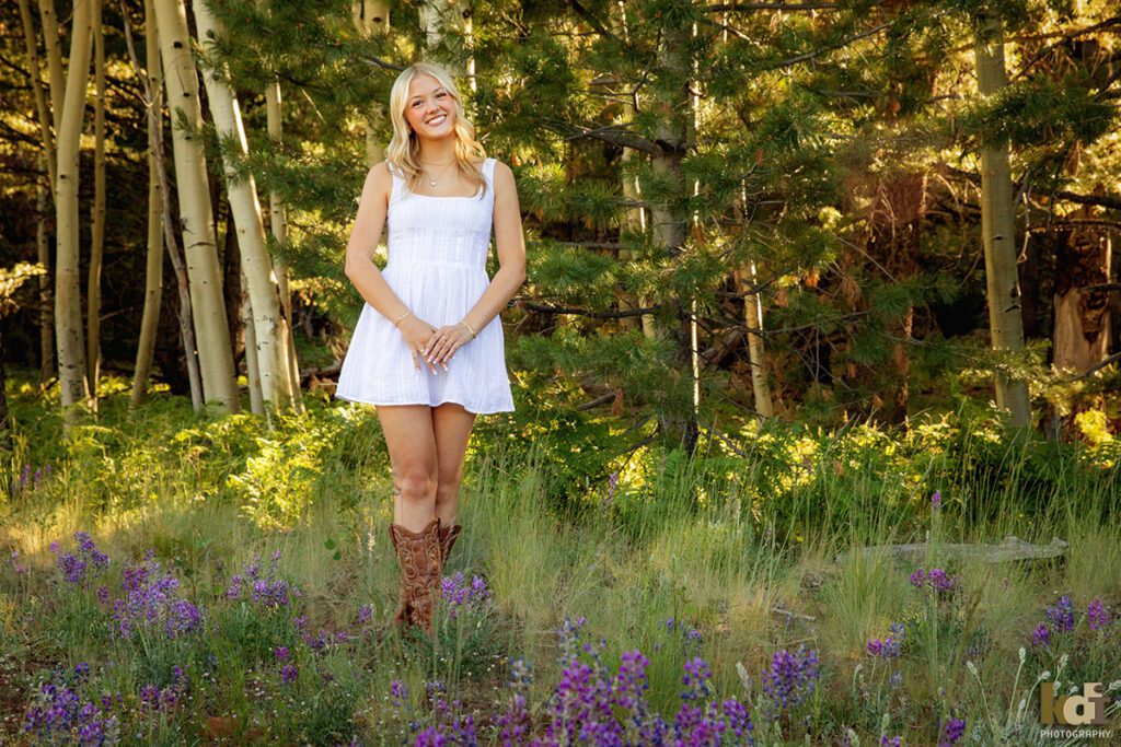 High school senior photos showing girl with blond hair, in white dress and cowboy boots, standing in purple lupine flowers, portrait photography in Flagstaff AZ by senior photographer KDI Photography