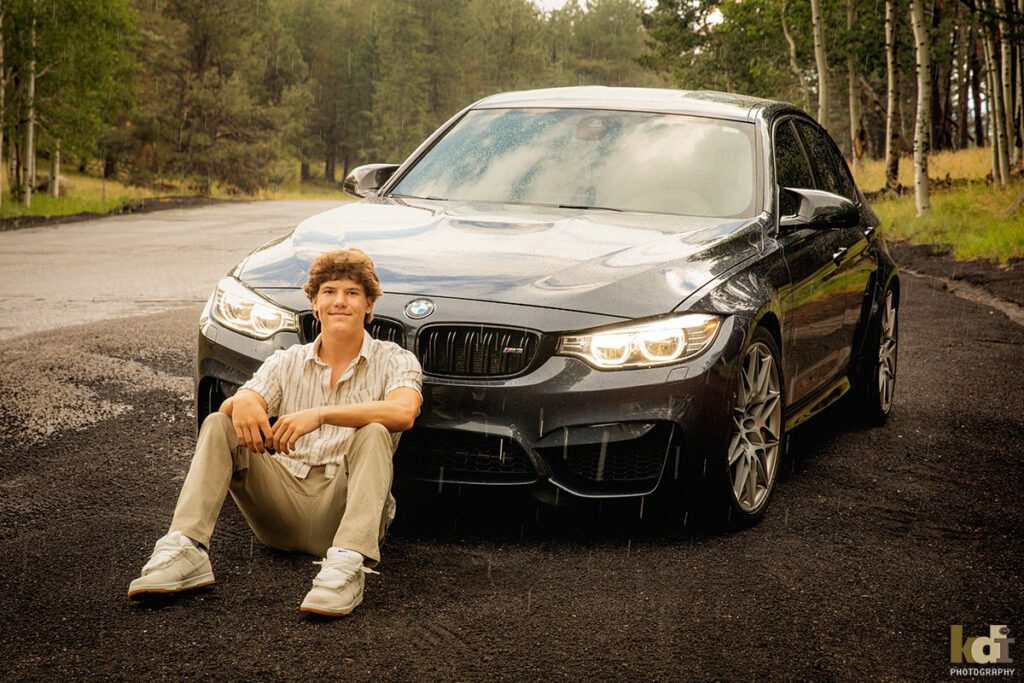 A young man sits contentedly, leaning against his car as the rain drops fall around him, senior photos on location in the San Francisco Peaks, by Flagstaff photographer, KDI Photography.