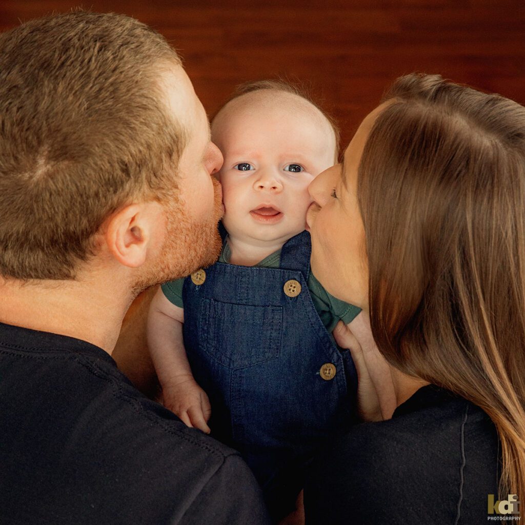 Color newborn photography, portrait of a new baby boy being kissed by his mother and father, in a photo studio in Flagstaff by newborn and family photographer, KDI Photography
