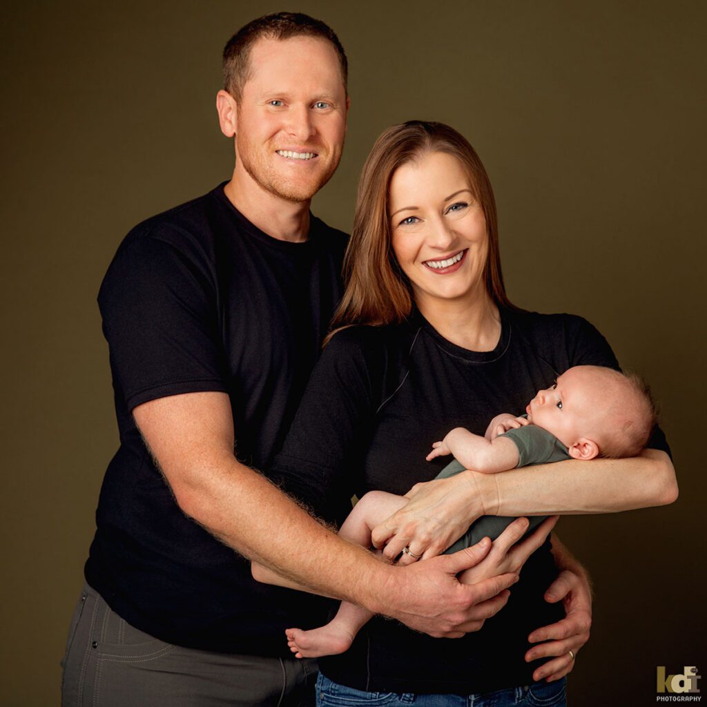 A mother and father smile as they hold their newborn baby boy, color newborn portrait of a new family in a photo studio in Flagstaff by newborn and family photographer, KDI Photography
