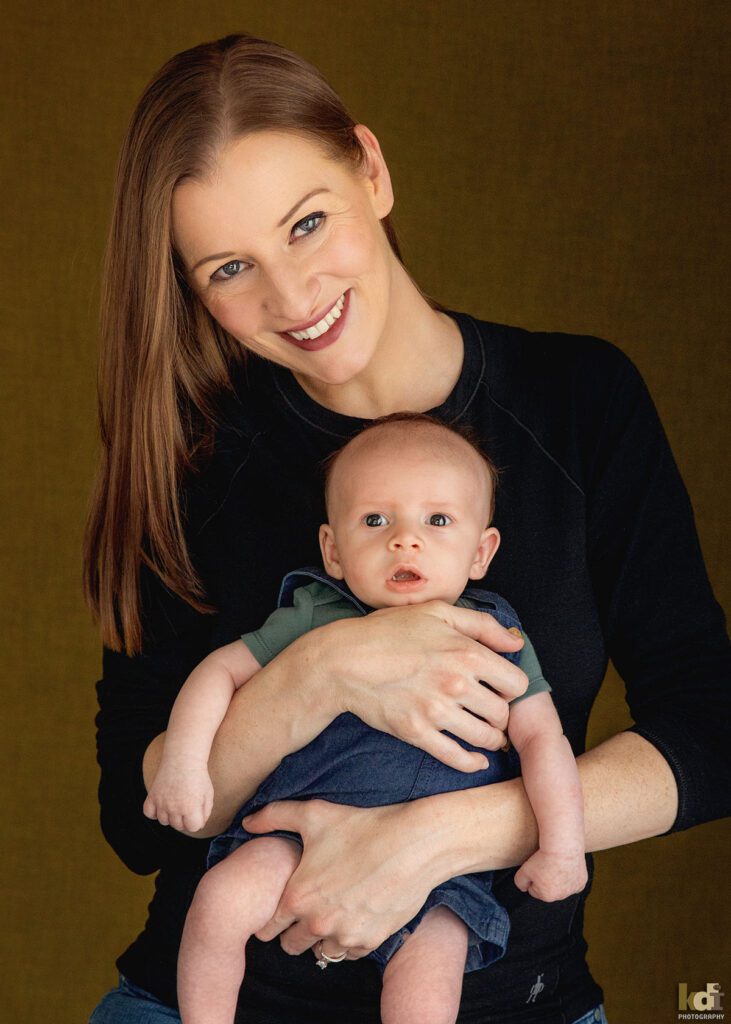 A mother smiles, holding newborn baby boy, color newborn portrait of a new family in a photo studio in Flagstaff by newborn and family photographer, KDI Photography
