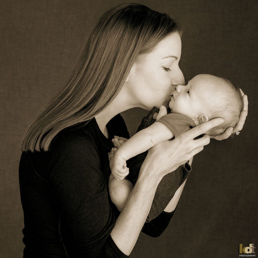 A mother holds and kisses her newborn baby boy, black and white newborn portrait of a new family in a photo studio in Flagstaff by newborn and family photographer, KDI Photography